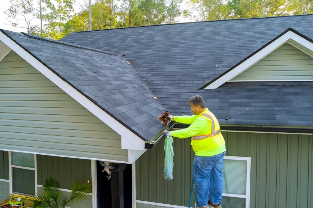 Worker is cleaning clogged roof gutter from dirt, debris fallen leaves to prevent water